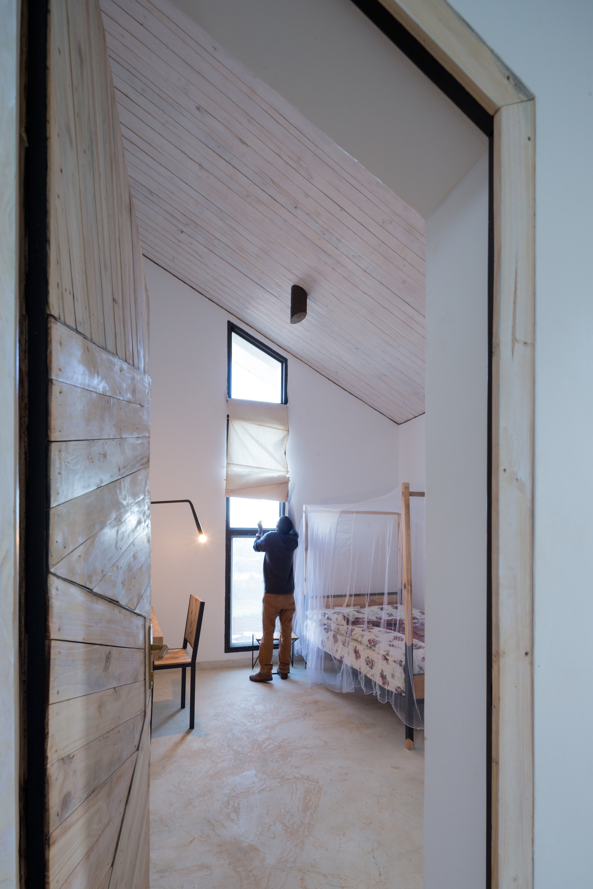 Photo of Butaro Doctors' Sharehousing, Photo by Iwan Baan, an Interior View of a Person adjusting a room's curtains